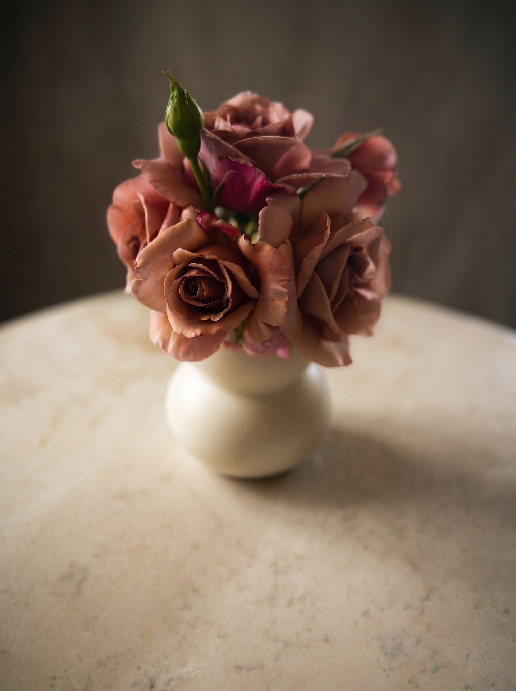 A small posy of Koko Loko roses in a cream ceramic vase, showing a range of mocha, blush, and dusty pink tones side by side.